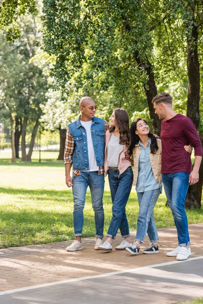 Amigos multiétnicos felices abrazándose mientras caminan juntos en el parque - foto de stock