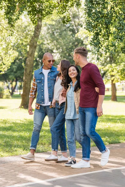 Lächelnde multiethnische Freunde, die sich beim gemeinsamen Spaziergang im Park umarmen — Stockfoto