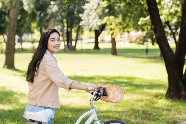 Cheerful pretty girl smiling while riding bicycle in park — Stock Photo