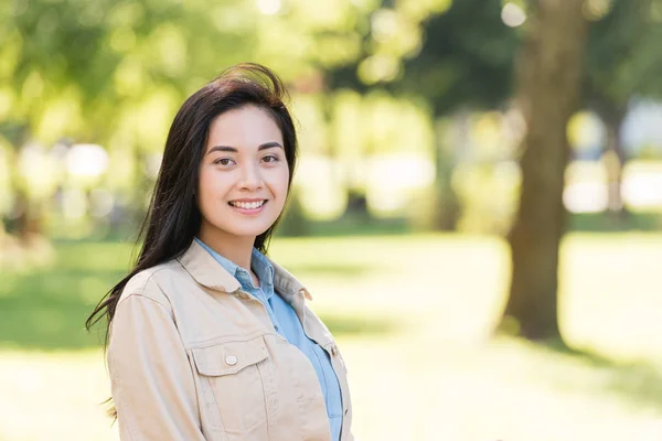 Cheerful young woman smiling while looking at camera in park — Stock Photo