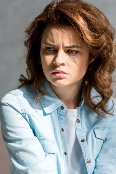 Worried curly woman in blue shirt looking away on grey — Stock Photo