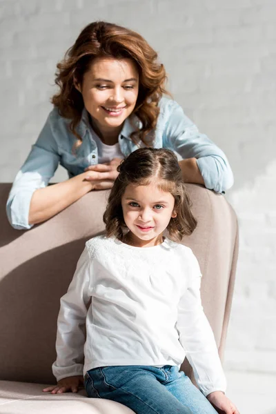 Mère et petite fille souriantes sur canapé gris — Photo de stock