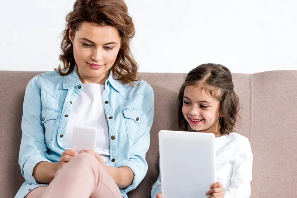 Mère et fille assis sur le canapé et utilisant smartphone et tablette numérique isolé sur blanc — Photo de stock