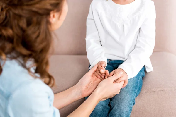 Partial view of child sitting on sofa and holding hands with mother — Stock Photo