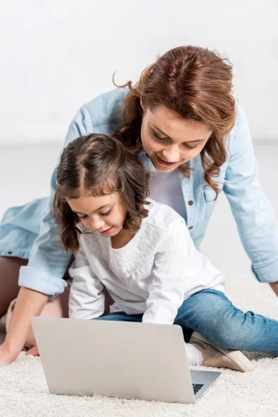 Sonriente madre y preescolar hija usando el ordenador portátil en blanco - foto de stock