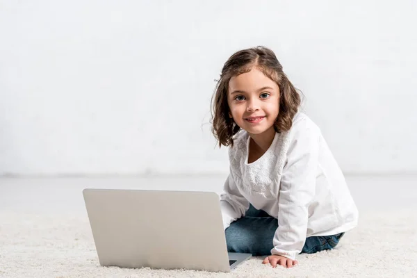 Niedliches Kind sitzt auf dem Boden und benutzt Laptop auf weiß — Stockfoto