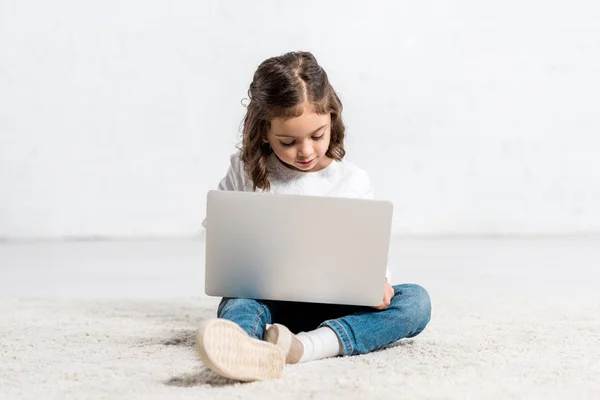 Concentrated preschooler kid using laptop while sitting on floor on white — Stock Photo