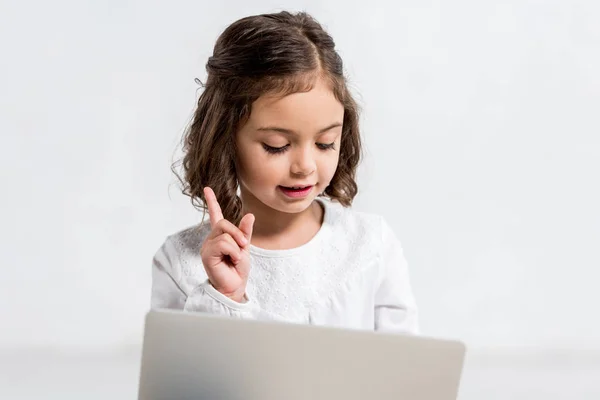 Miúdo bonito apontando com o dedo ao usar laptop no branco — Fotografia de Stock