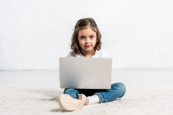 Adorable kid sitting on floor and using laptop on white — Stock Photo