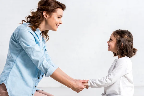 Mère et fille souriantes se tenant la main et se regardant sur le blanc — Photo de stock