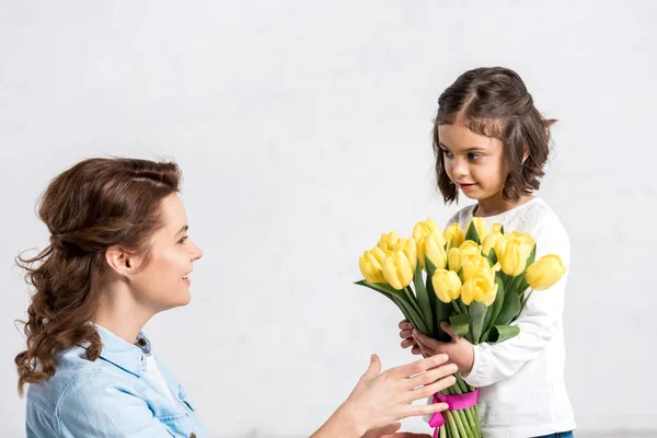 Carino bambino che presenta tulipani gialli a madre isolata su bianco — Foto stock