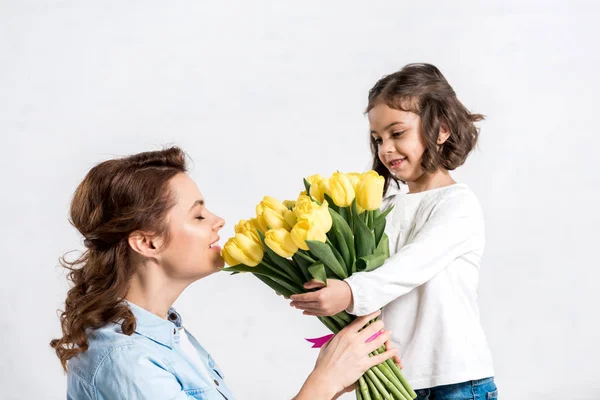 Smiling mother sniffing yellow tulips from daughter isolated on white — Stock Photo