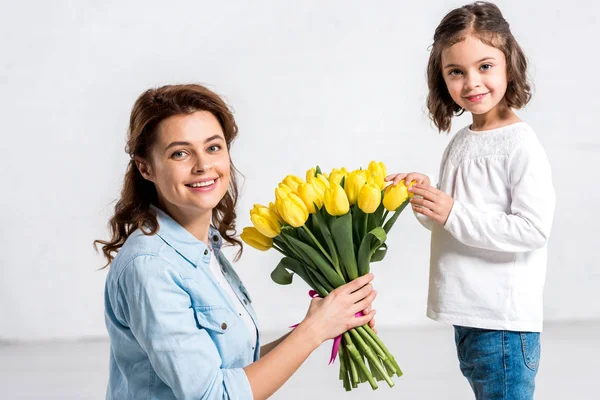 Happy mother holding bouquet of yellow tulips from daughter on white — Stock Photo