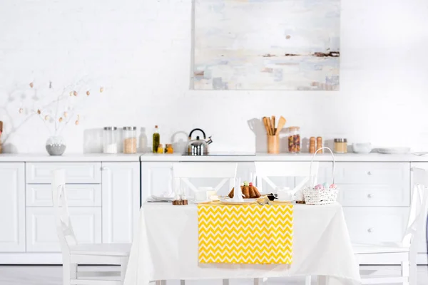 Стол с желтой скатертью, пасхальный торт и посуда на кухне — стоковое фото