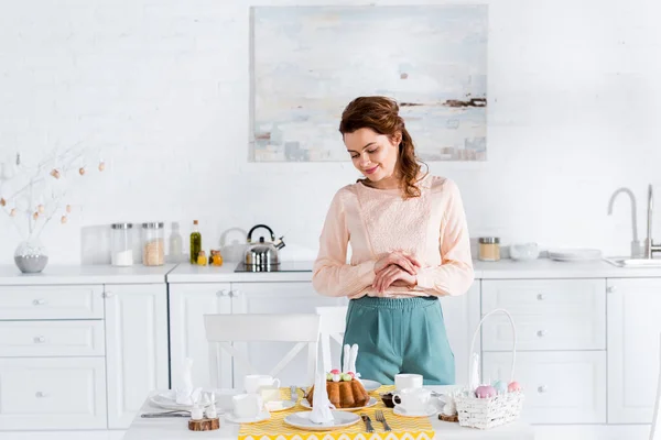 Mujer feliz mirando pastel de Pascua en la mesa en la cocina - foto de stock