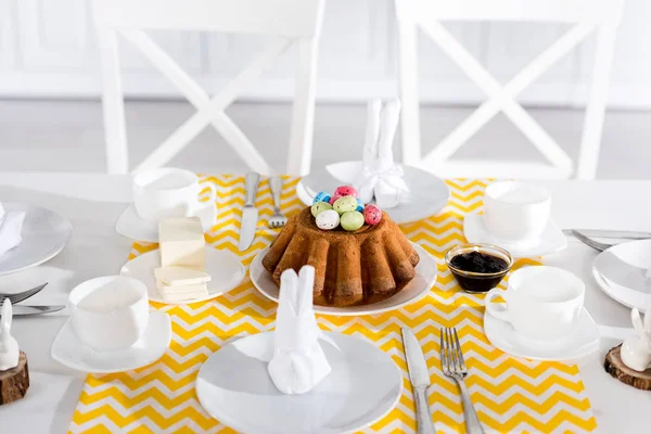 Пасхальный торт с покрашенными яйцами и посудой на столе — стоковое фото