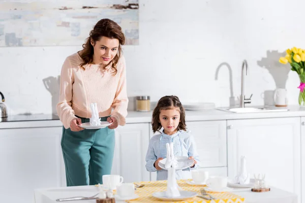 Curly mother and cute preschooler daughter serving table together — Stock Photo