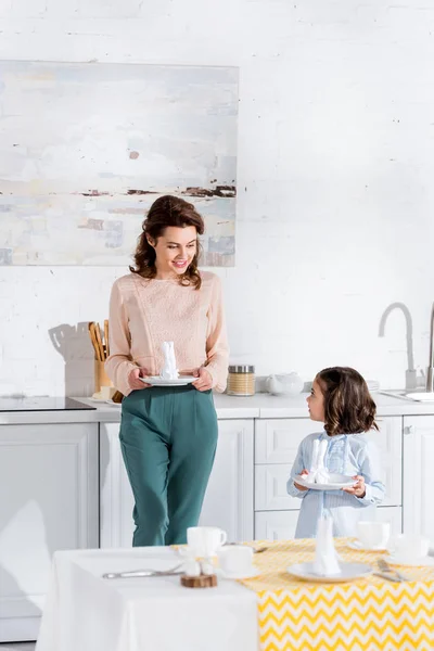 Madre e hija mirándose mientras sirven la mesa - foto de stock