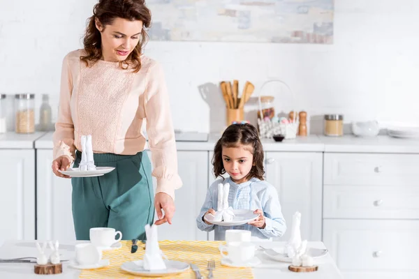 Curly mãe e filha pré-escolar servindo mesa na cozinha — Fotografia de Stock