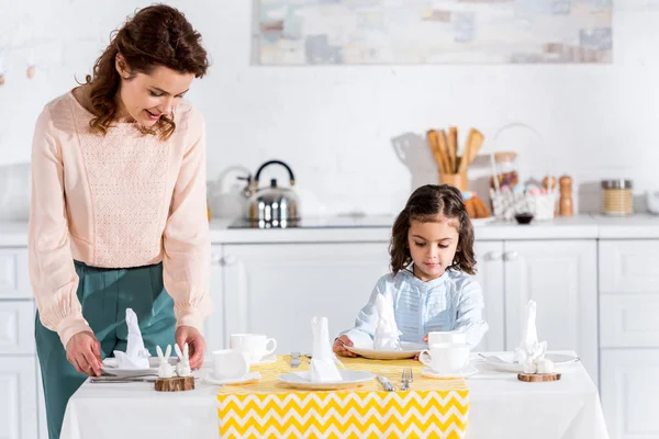 Mère et petite fille servant une table avec des serviettes dans la cuisine — Photo de stock