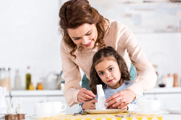 Mère et petite fille souriantes pliantes serviettes dans la cuisine — Photo de stock