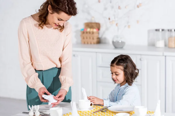 Lächelnde Mutter und Tochter falten weiße Servietten in der Küche — Stockfoto