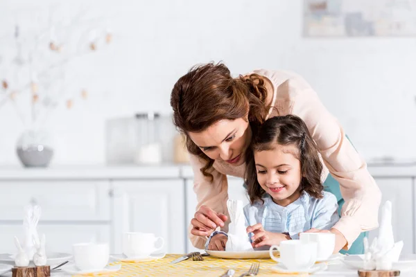 Мати і маленька дочка розкладають серветки за столом на кухні — стокове фото