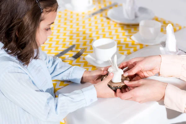 Vista recortada de madre e hija sosteniendo conejito de cerámica en la mesa - foto de stock