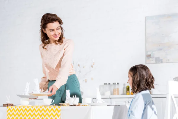Charmante Frau schaut Tochter lächelnd an, während sie Tisch dekoriert — Stockfoto