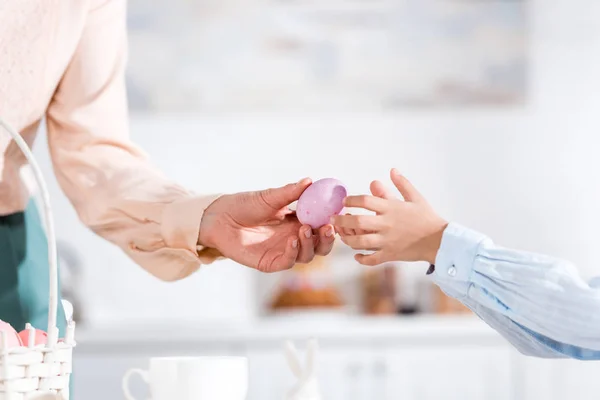 Vista parcial de la mujer dando huevo de Pascua pintado al niño - foto de stock