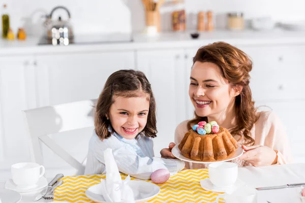 Laughing mother and daughter serving table with easter in kitchen — Stock Photo