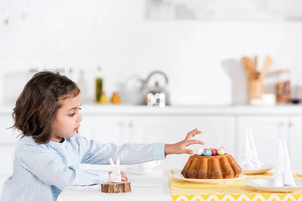 Bambino adorabile che decora il pane pasquale con uova dipinte in cucina — Foto stock