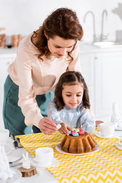 Mère et fille décorer gâteau de Pâques avec des œufs peints dans la cuisine — Photo de stock