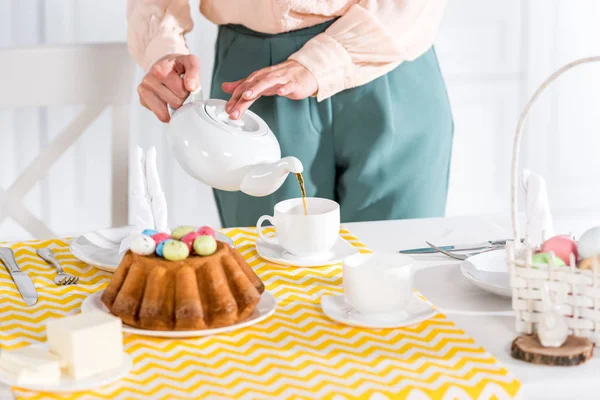 Vista ritagliata della donna con teiera versare il tè in tazza sul tavolo — Foto stock