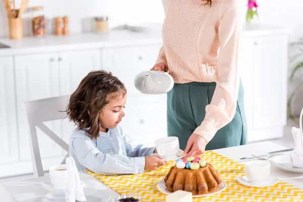 Vista recortada de la mujer sosteniendo la tetera y dando taza a la hija - foto de stock