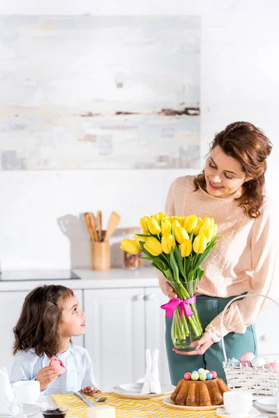 Enfant mangeant macaron et regardant la mère avec bouquet de tulipes dans la cuisine — Photo de stock