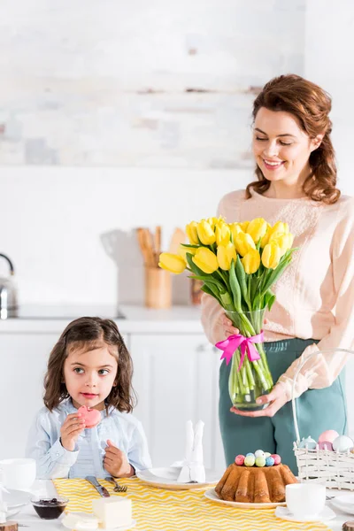 Мама держит букет тюльпанов и смотрит на дочь возле пасхального стола — стоковое фото