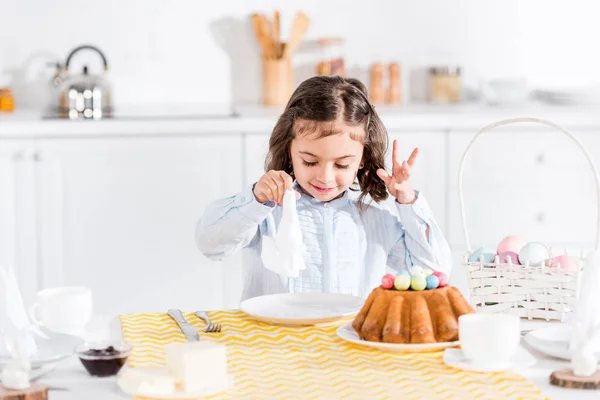 Criança sorridente sentada à mesa com bolo de Páscoa e guardanapo — Fotografia de Stock