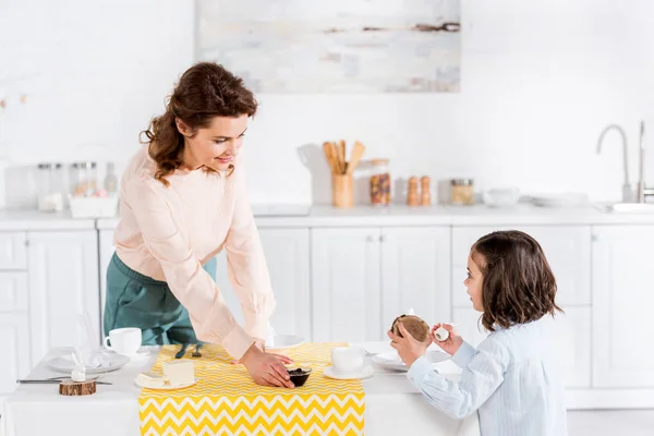 Alegre encaracolado mãe e filha servindo mesa na cozinha — Fotografia de Stock
