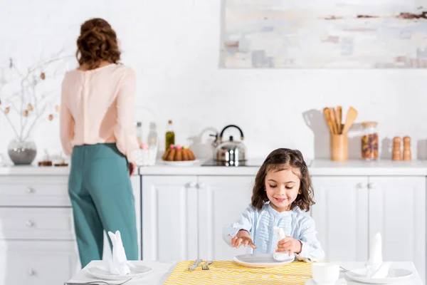 Smiling preschooler kid folding napkin at table in kitchen — Stock Photo