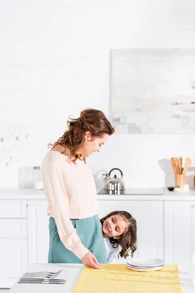 Fille et mère souriantes debout près de la table dans la cuisine — Photo de stock