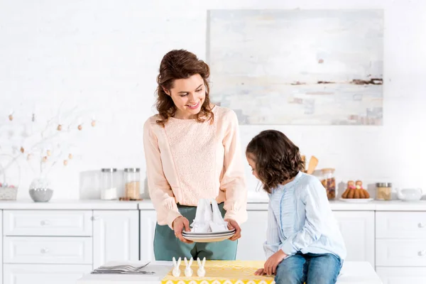 Mère souriante montrant des serviettes pliées à la fille dans la cuisine — Photo de stock