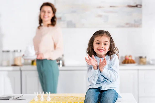 Радостный ребенок сидит на столе и улыбается на кухне — стоковое фото