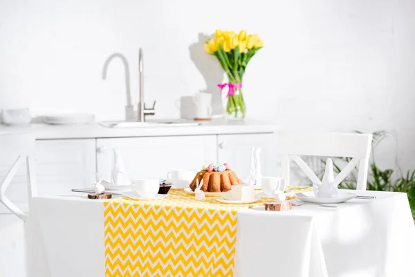 Table de service avec gâteau de Pâques, serviettes et lapins en céramique dans la cuisine — Photo de stock