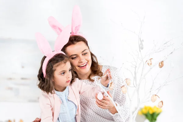 Mère et fille bénies dans des oreilles de lapin décorant l'arbre de Pâques — Photo de stock