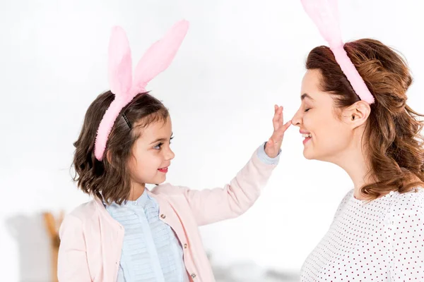 Mãe feliz e filha em orelhas de coelho jogando no branco — Fotografia de Stock