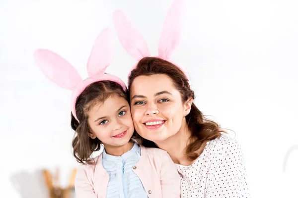 Усміхнена мати і дочка у вухах кролика дивиться на камеру на білому — стокове фото