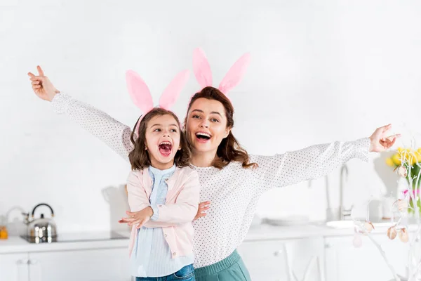 Смеющаяся мать и дочь в кроличьих ушах веселятся на кухне — стоковое фото