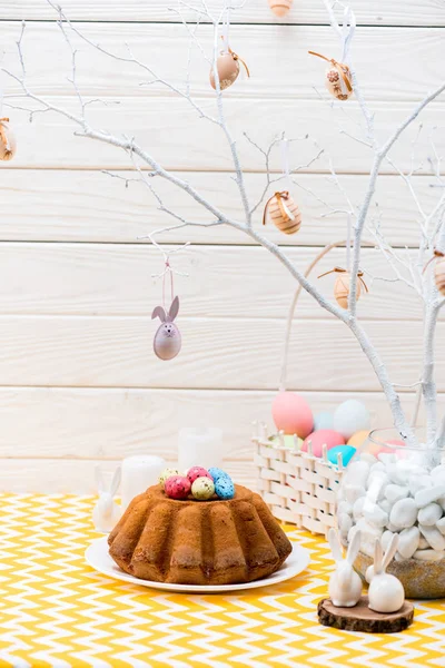 Пасхальный торт с покрашенными яйцами и керамическими кроликами на столе — стоковое фото