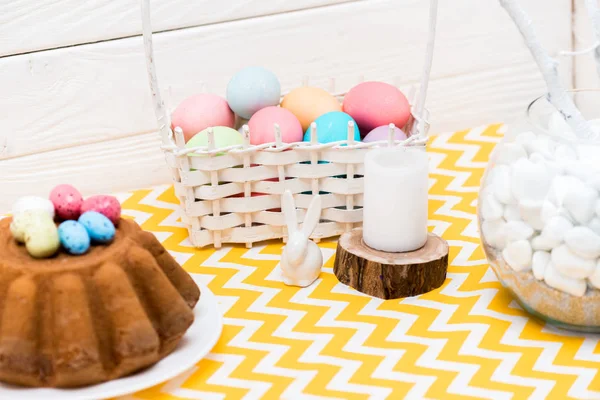 Torta pasquale, uova dipinte, candela e coniglietto in ceramica sul tavolo — Foto stock